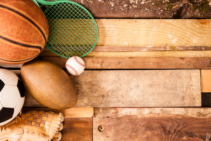 Sports concept. Basketball, tennis racket, baseball, glove, soccer ball, football to left of unique wooden boards background. Selective focus on wooden boards.