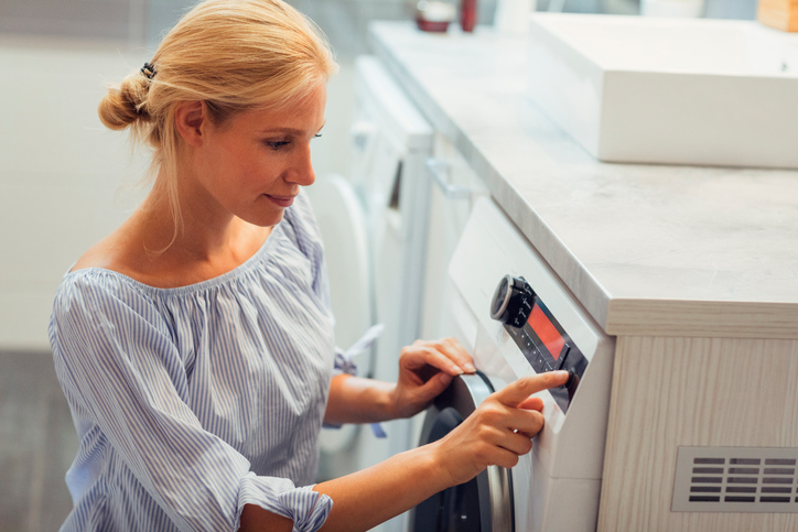 Mid adult woman doing laundry. Turning on or off washing machine.