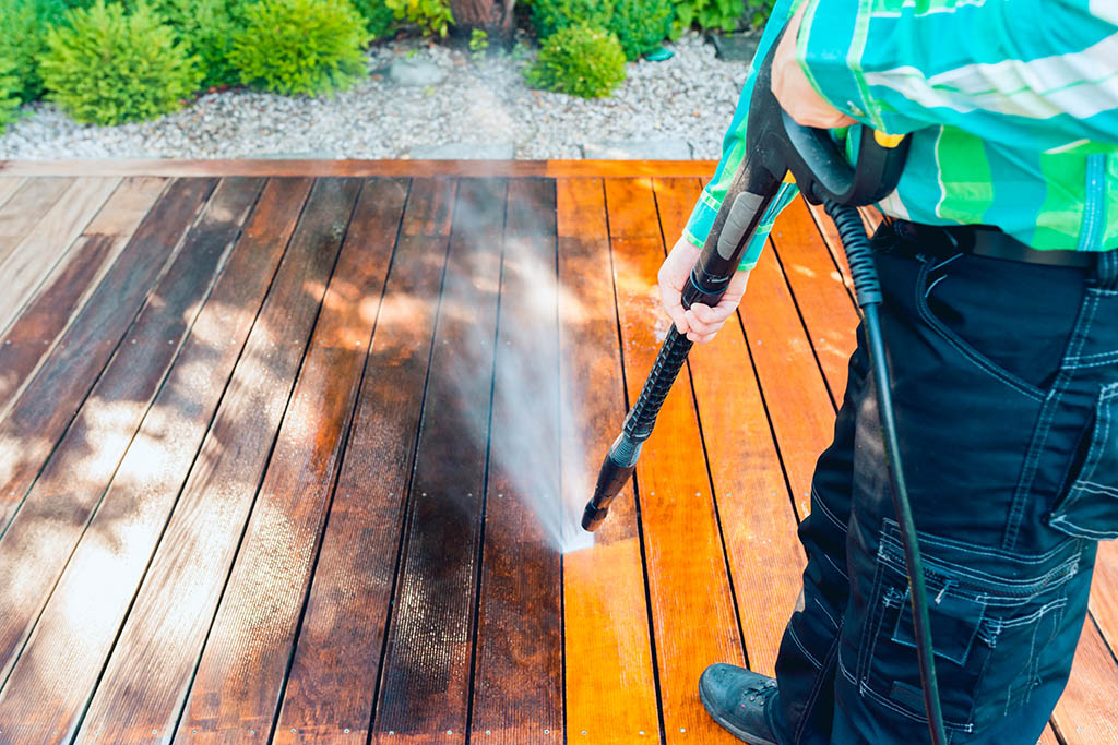 power washing man cleaning terrace with a power washer high water pressure cleaner on wooden terrace surface
