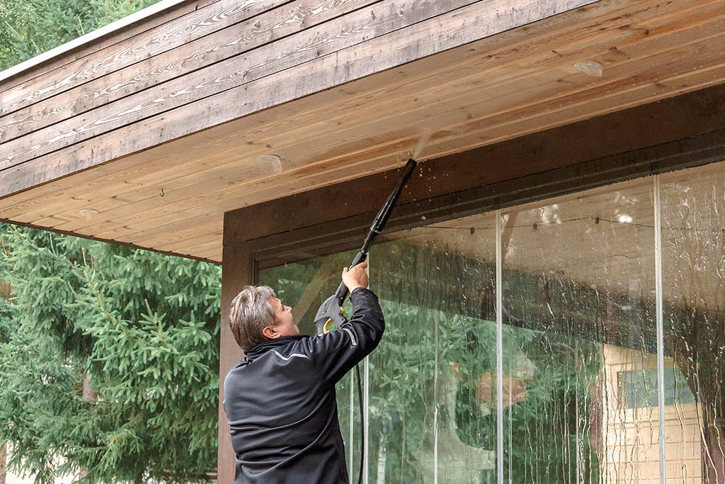 Man cleaning walls and floor with high pressure power washer. Washing terrace wood planks and cladding walls.