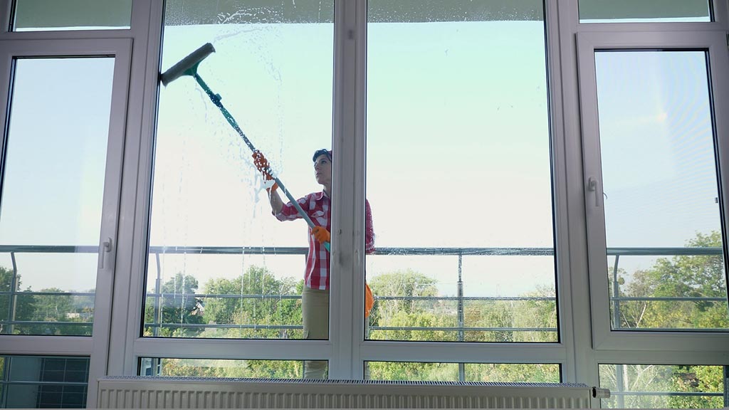 smiling Caucasian Beautiful woman, housewife or Cheerful female worker of cleaning service, in gloves, Cleaning, washing Windows by special mop, enjoying her work. Cleaning lady